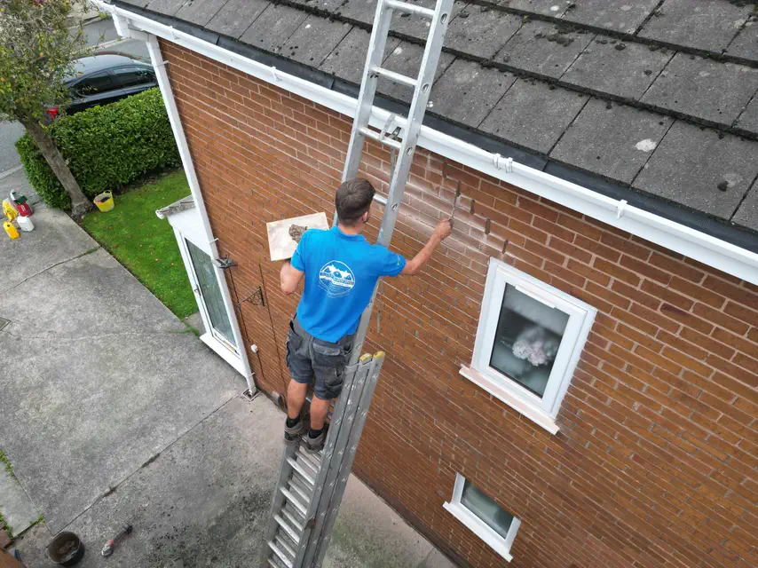 One of the ASAP Roofing team on a ladder at the gable end of a brick house