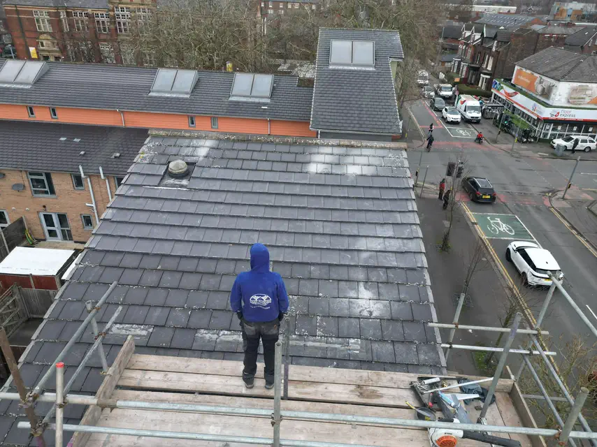 One of the ASAP Roofing team standing on the scaffold above a grey tiled roof on a street corner