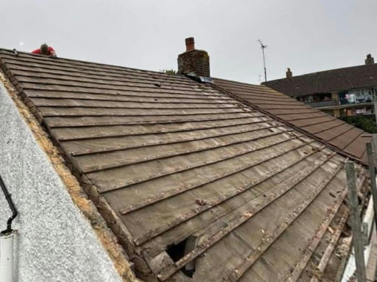 Worn concrete roof tiles, broken and gappy along the gable edge, before the re-roof