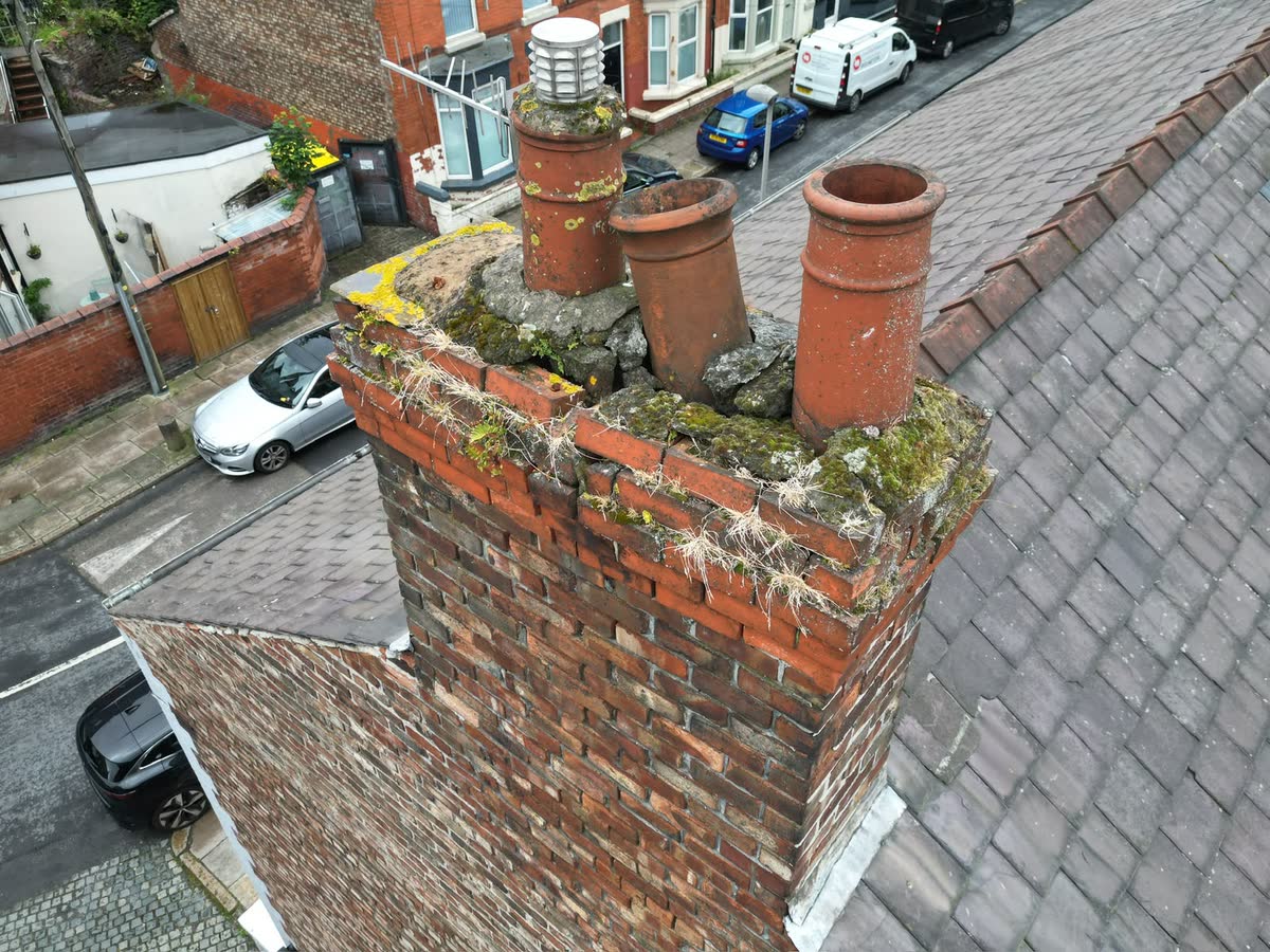 An old brick chimney stack with three clay pots and moss on the top