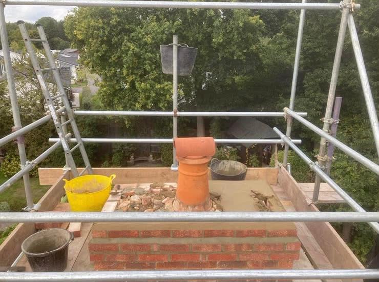 A chimney being rebuilt inside the scaffold, with a new clay pot