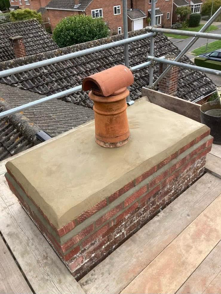 A rebuilt brick chimney with a new cement cap and clay pot