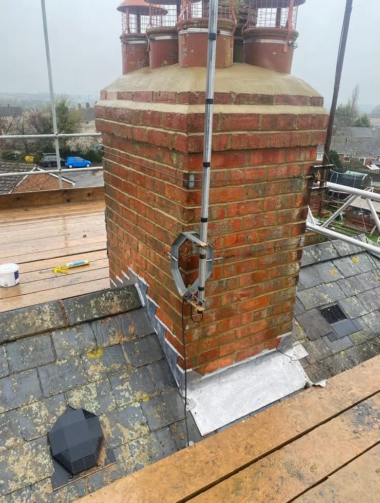 A tall brick chimney stack with clay pots, seen from the scaffold