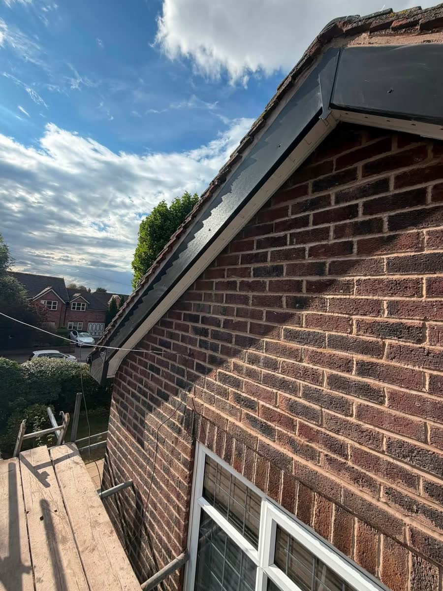 New black fascia along a brick gable, with the scaffold below