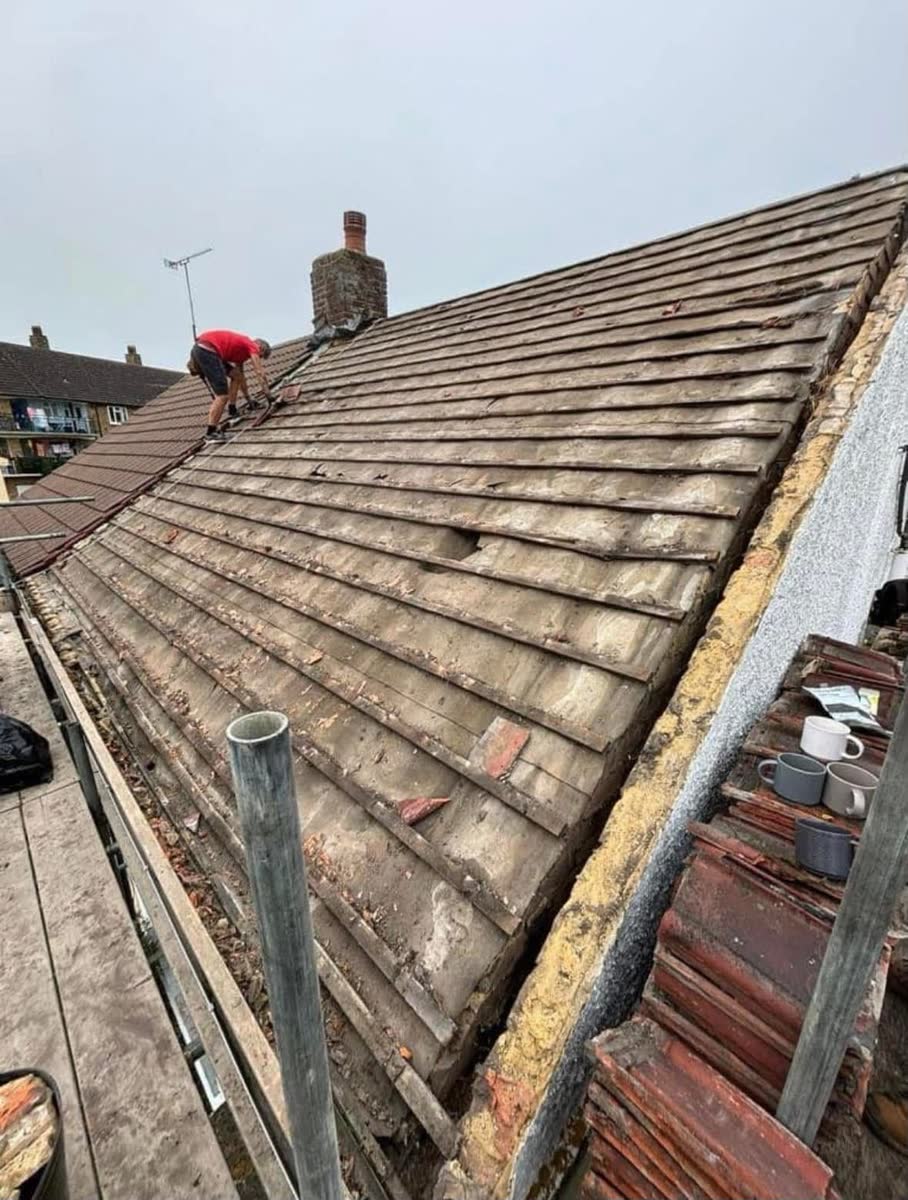 An old tiled roof part stripped, with one of the team working up at the ridge