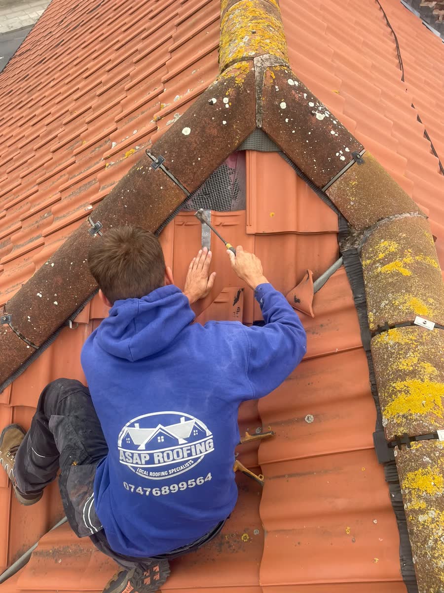 One of the ASAP Roofing team repairing tiles under the ridge of a red tiled roof