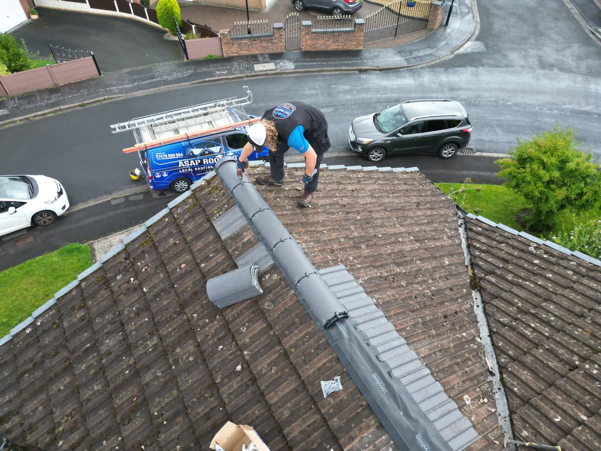 One of the team working along the ridge of a concrete tiled roof, the van parked below